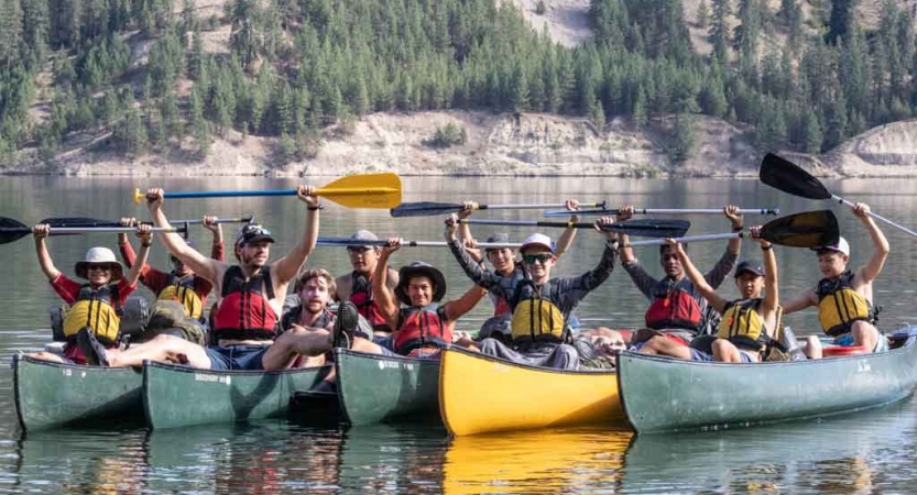 a group of boys sitting in canoes raise their paddles in the air in celebration on an outward bound course